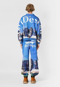 Sudadera gráfica azul con estampado de montañas, texto grande y pantalones azules a juego con estampado, combinados con botas marrones.