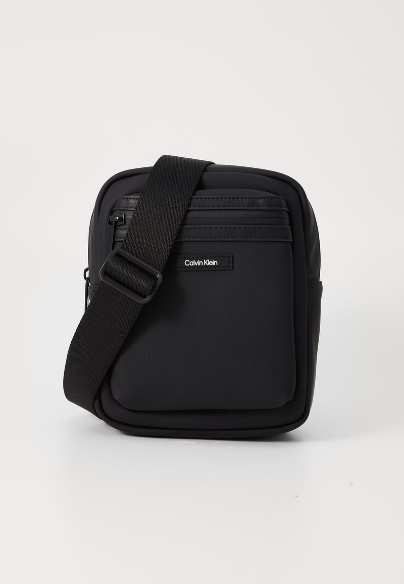 Borsa a tracolla nera in nylon con texture liscia, tasche con cerniera e tracolla regolabile. Presenta il logo Calvin Klein sul davanti.