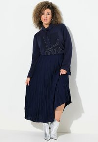 Felpa navy con cappuccio decorata con il testo "LOVE" in argento, abbinata a una lunga gonna navy plissettata e stivaletti argento alla caviglia.