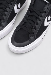 Baskets en toile noire avec une semelle en caoutchouc, décorées d'une étoile blanche et d'accents en chevrons, lacets plats et texture supérieure lisse.