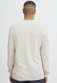 Suéter de punto suave en color beige claro, con cuello redondo, mangas largas y ribetes en el dobladillo y las mangas.