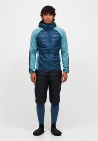 Heren geïsoleerde jack en gewatteerde broek. Blauwe en teal kleurstelling, geborduurd textuur op de jas, gestroomlijnd ontwerp, met capuchon en elastische manchetten.