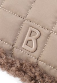 Tissu matelassé beige avec une bordure en fausse fourrure texturée marron. Présente une lettre "B" en relief marron affichée de manière proéminente.