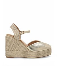 Sandalias de cuña con una puntera metálica dorada, plataforma de yute trenzado y una correa de tobillo a cuadros. Esquema de colores en beige y dorado.