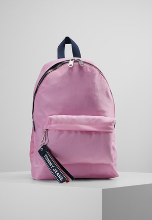 Pink rygsæk med forlommes lynlås og navyblåt håndtag, med en sort nøgleringsmærkat med teksten "Tommy Jeans" hængende fra lynlåsen.