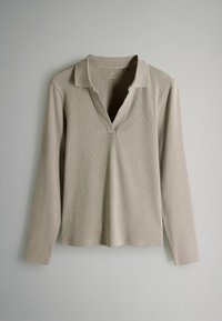 Jasno beżowa koszulka polo z długim rękawem, z dekoltem w kształcie litery V i prążkowaną fakturą. Posiada klasyczny kołnierz oraz luźny krój.