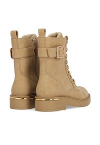 Beige semišové kotníkové boty se zipem na boku, šněrováním vpředu a blokovým podpatkem s zlatým akcentem. Obsahují detail s přezkou.