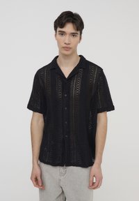 Maglietta nera a maniche corte in maglia con chiusura a bottoni sul davanti, caratterizzata da un motivo tessuto a intaglio e un design del colletto rilassato.
