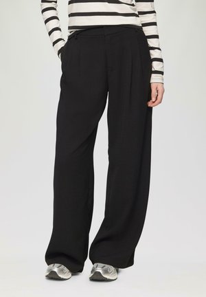 Black wide-leg trousers with a high waist, pleats, and a smooth texture, paired with silver athletic shoes and a striped long-sleeve top.