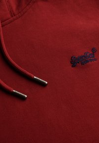 Felpa rossa con cappuccio realizzata in morbido tessuto, con un logo ricamato e coulisse con terminali in metallo impressi con la scritta "SUPERDRY."