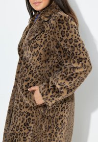 Leopardprint faux fur frakke med en blød tekstur, brede klapper, lange ærmer og sidelommer, prydet med brune og sorte mønstre på en lys baggrund.