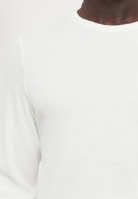 Cămașă albă cu mâneci lungi, texturată, cu un model cu nervuri și un guler contrastant. Țesătura pare ușoară și respirabilă.