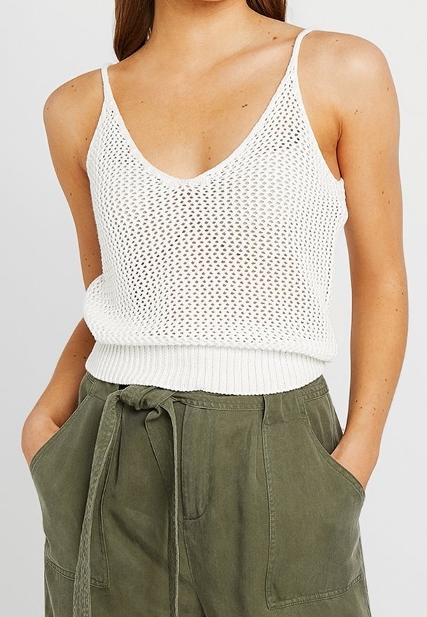 Débardeur blanc en maille sans manches avec un col en V et un motif ajouré, associé à un pantalon vert à cordon de serrage.