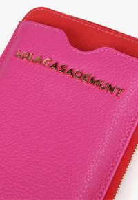 Cartera de cuero rosa con acabado texturizado, que presenta un logo dorado "LOLA CASADEMUNT" y un bolsillo con cremallera interior rojo.