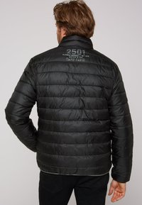 Giacca a vento nera con design trapuntato. Sul retro sono presenti i loghi "2501 ALASKA" e "CAMP DAVID" in grigio. Texture liscia e lucida.