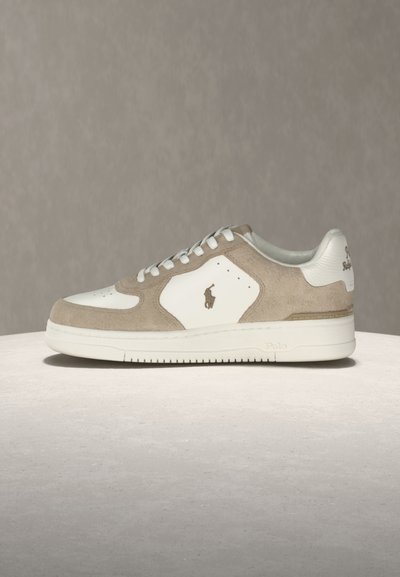 Λευκό και μπεζ αθλητικό παπούτσι χαμηλού τύπου με λευκά κορδόνια, λαστιχένια σόλα και λογότυπο Polo στο πλάι και στη φτέρνα, τοποθετημένο σε ανοιχτόχρωμη επιφάνεια.