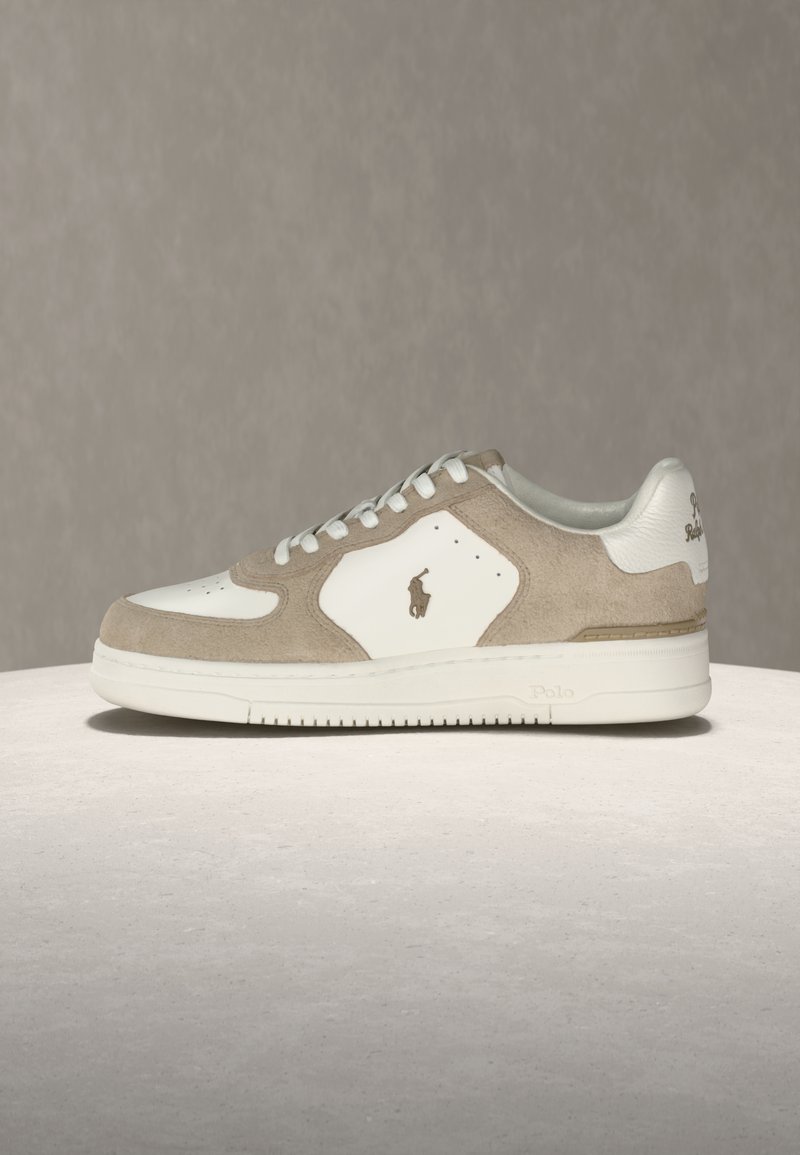 Pantof sport bej și alb, cu talpă din cauciuc, șireturi albe și logo Polo pe lateral și pe călcâi, expus pe o suprafață deschisă la culoare.