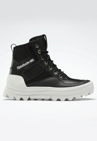 Black high-top sneaker with leather and mesh materials, featuring a white thick sole and lacing system. Reebok logo on the side.