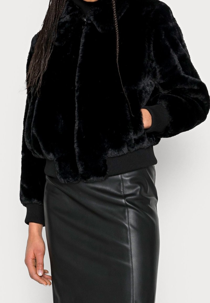 Sort faux fur bomberjakke med ribbede manchetter og kant. Glat tekstur, rund krave og lynlås lukning. Bæres med en sort lædernederdel.