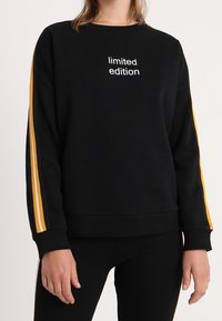 Sweatshirt noir avec le texte « édition limitée », présentant des détails à rayures jaunes le long des manches. Fabriqué en tissu doux avec une coupe décontractée.