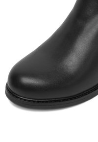 Čierna kožená členková obuv s okrúhlou špičkou, hladkou textúrou, minimalným šitím a plochou podrážkou so slabým lesklým povrchom.
