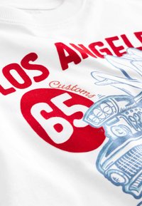 Balta T-kreklu ar sarkano un zilo tekstu. Dizains ietver "LOS ANGELES", automašīnas grafiku un "65" treknās burtās. Mīksta auduma tekstūra.