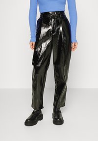 Calças pretas, brilhantes, de cintura alta com um design de pernas largas. Combinadas com uma blusa azul justa de mangas compridas e botas pretas robustas.