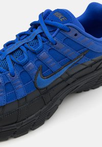 Blue Nike sneaker featuring a mesh and suede upper, black rubber sole, prominent stitching, and a logo in dark blue on the side.