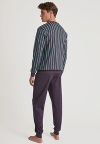 Mannelijke loungewear set met een gestreept, donker bovenstuk met lange mouwen en bijpassende effen paarse broek. Gemaakt van zachte stof.