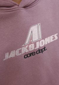 Hoodie violet avec le nom de la marque "JACK & JONES" et le texte "core dept." dans des couleurs contrastantes. Texture du tissu douce visible.