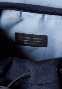 Námořnická tkanina s hladkou strukturou, na které je kožená visačka s nápisem "United Colors of Benetton" a "Designed in Italy" ve stříbrném písmu.