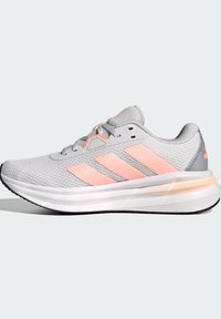 Zapatilla deportiva gris con acentos en rosa. Parte superior de malla, suela intermedia blanca gruesa, logo de tres franjas en el costado y suela texturizada.