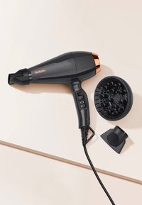 Zwarte BaByliss-haardroger met bedieningsknoppen, netsnoer, diffuser en geconcentreerde mondstuk op een beige oppervlak.