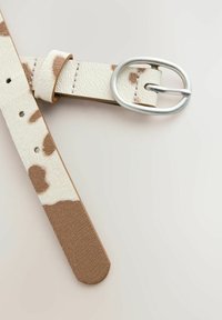 Ceinture en cuir couleur crème avec des taches brunes irrégulières, boucle ovale en argent et détails cousus sur un fond neutre.