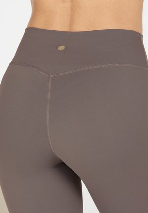 Hochtaillierte Leggings aus einem gedämpften braunen Stoff. Glatte Textur mit kontrastierenden Nähten und einem kleinen Logodetail in der Nähe des Taillenbunds.