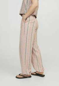 Gestreepte lichtgewicht broek met een ontspannen pasvorm, voorzien van verticale strepen in roze, beige en zwart, en zijzakken. Gecombineerd met zwarte slippers.
