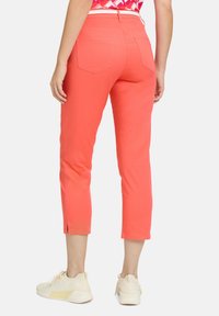 Pantalons capri corail au design ajusté. Dotés de poches arrière et de fentes aux chevilles. Associés à des chaussures de sport beiges claires.