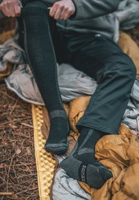 Medias negras hasta la rodilla con refuerzo en el talón y la puntera, tejido texturizado, sutiles acentos grises, utilizadas con pantalones oscuros sobre un saco de dormir.