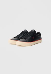 Μαύρα δερμάτινα αθλητικά παπούτσια με στρογγυλερή μύτη, μαύρη δαντέλα, ανάγλυφη κρέμ ελαστική σόλα και κόκκινη λεπτομέρεια κατά μήκος της μεσαίας σόλας.