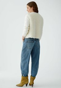 Crème kunstbont jack met lange mouwen, gecombineerd met loose blue denim jeans en mosterdgele enkellaarsjes met punten hakken.