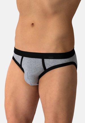 Männlicher Torso trägt graue gerippte Slionslips mit schwarzem Bund und Besatz vor einem schlichten hellen Hintergrund.