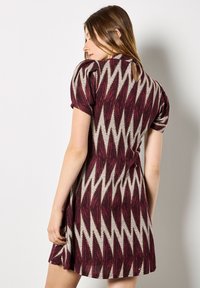 Robe à manches courtes en bordeaux et gris avec des motifs en zigzag, texture douce et détail en forme de clé au dos, s'évasant doucement à l'ourlet.