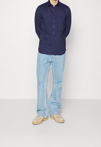 Camicia navy con bottoni, maniche lunghe, dal tessuto liscio e bottoni neri, abbinata a jeans azzurri a zampa d'elefante e scarpe color sabbia.
