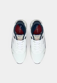 Baskets de sport blanches avec une tige texturée, des accents en mesh et une semelle en caoutchouc, avec des détails bleus et rouges sur la semelle intérieure et le marquage.