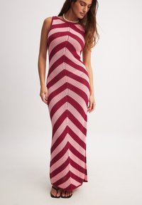 Kootud maksikleit punaste ja roosa chevroniribadega, ilma varrukateta disain ja sobiv vorm. Omab tekstureeritud kangast ja avatud kudet.