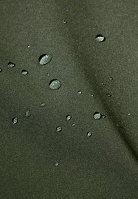 Tessuto impermeabile verde scuro con una consistenza liscia, caratterizzato da gocce d'acqua sparse sulla superficie, che evidenziano la sua qualità idrorepellente.
