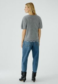 Grijze mohair-mix trui met korte pofmouwen en kantafwerking aan de zoom, gecombineerd met blauwe denim jeans en zwarte enkellaarsjes met een hak.