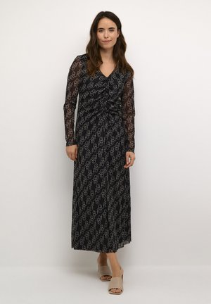 Langes schwarzes Kleid mit transparenten langen Ärmeln, das ein sich wiederholendes geometrisches Muster in Weiß aufweist. Drapiertes Design mit gerafftem Taillendetail.