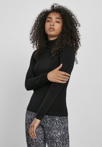 Fekete garbós pulóver hosszú ujjakkal. Textúrált kötött anyag. Mintás leggings-szel párosítva, amelyek szürke és fehér dizájnnal rendelkeznek.