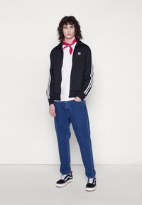 Black zip-up athletic jacket with white stripes, white T-shirt, blue denim jeans, and black sneakers. Red bandana tied around the neck.